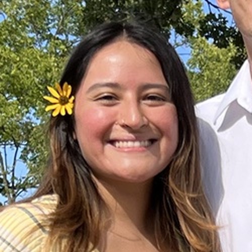 Cynthia smiling outdoors with a yellow flower in her hair